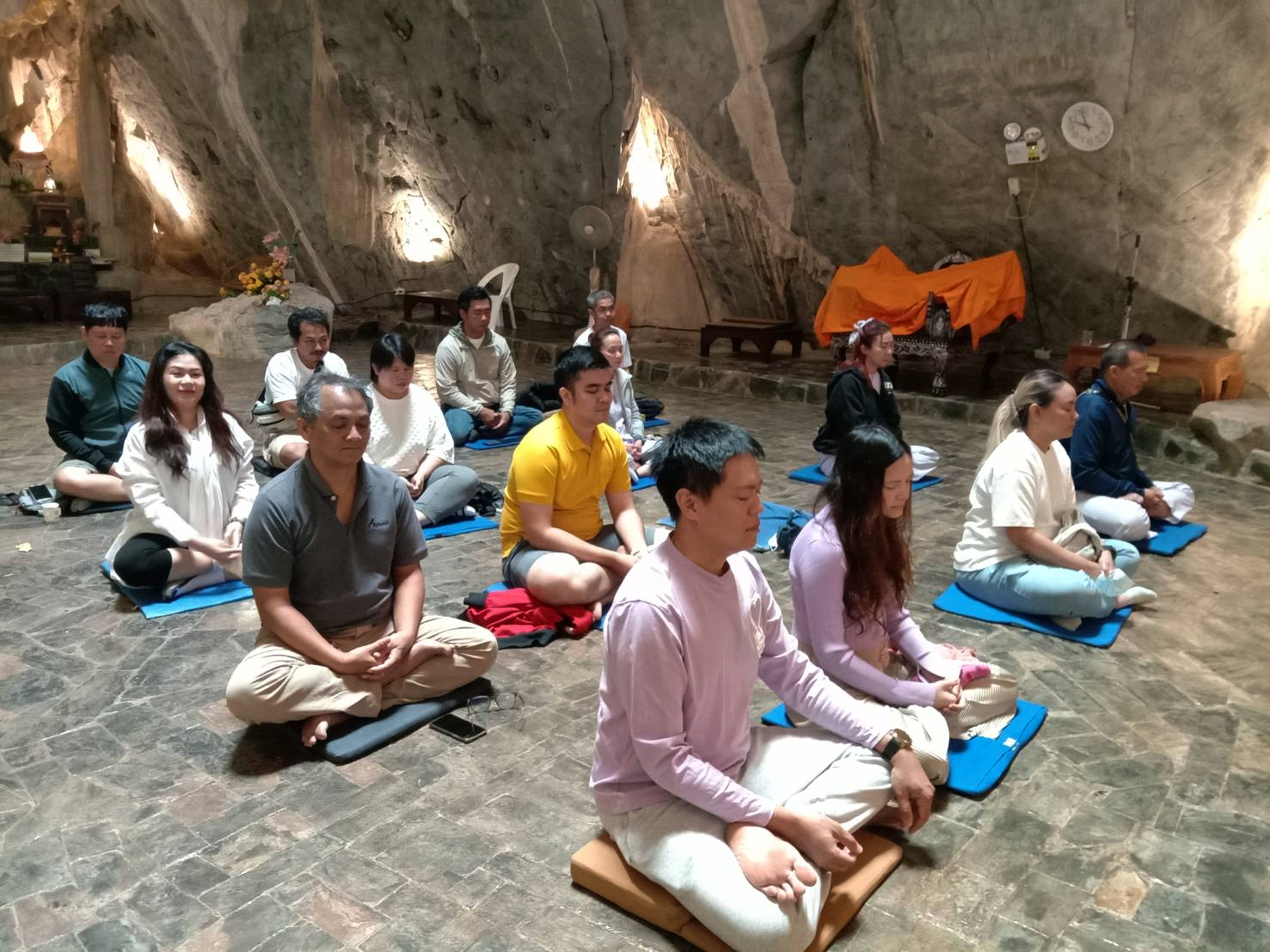 กลุ่มผู้ปฏิบัติธรรมนั่งขัดสมาธิบนเบาะรองในศาลาถ้ำ