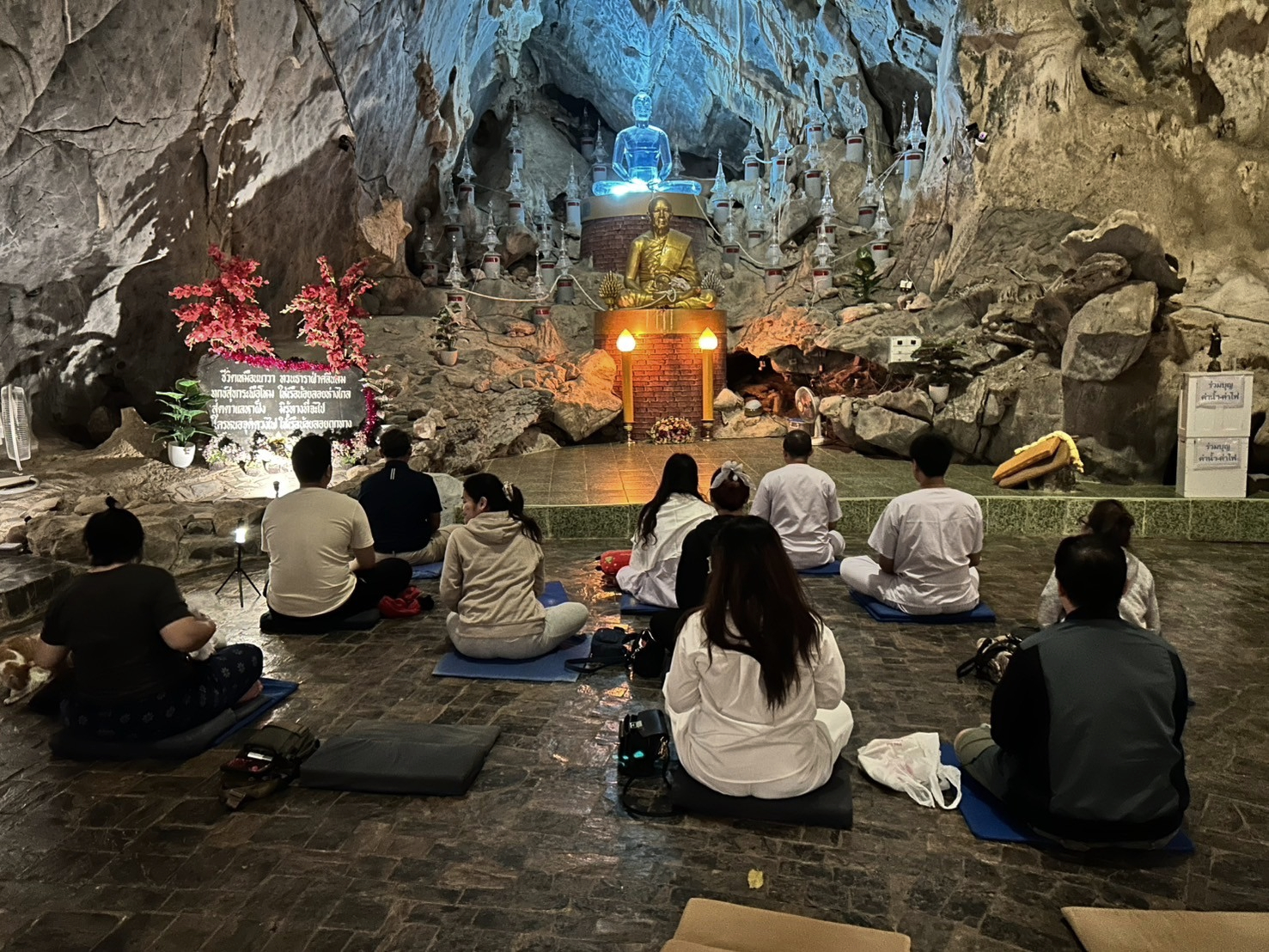ผู้ปฏิบัติธรรมนั่งสมาธิภายในถ้ำ เบื้องหน้าเป็นรูปเหมือนพระเกจิสีทองและพระแก้วสีฟ้า