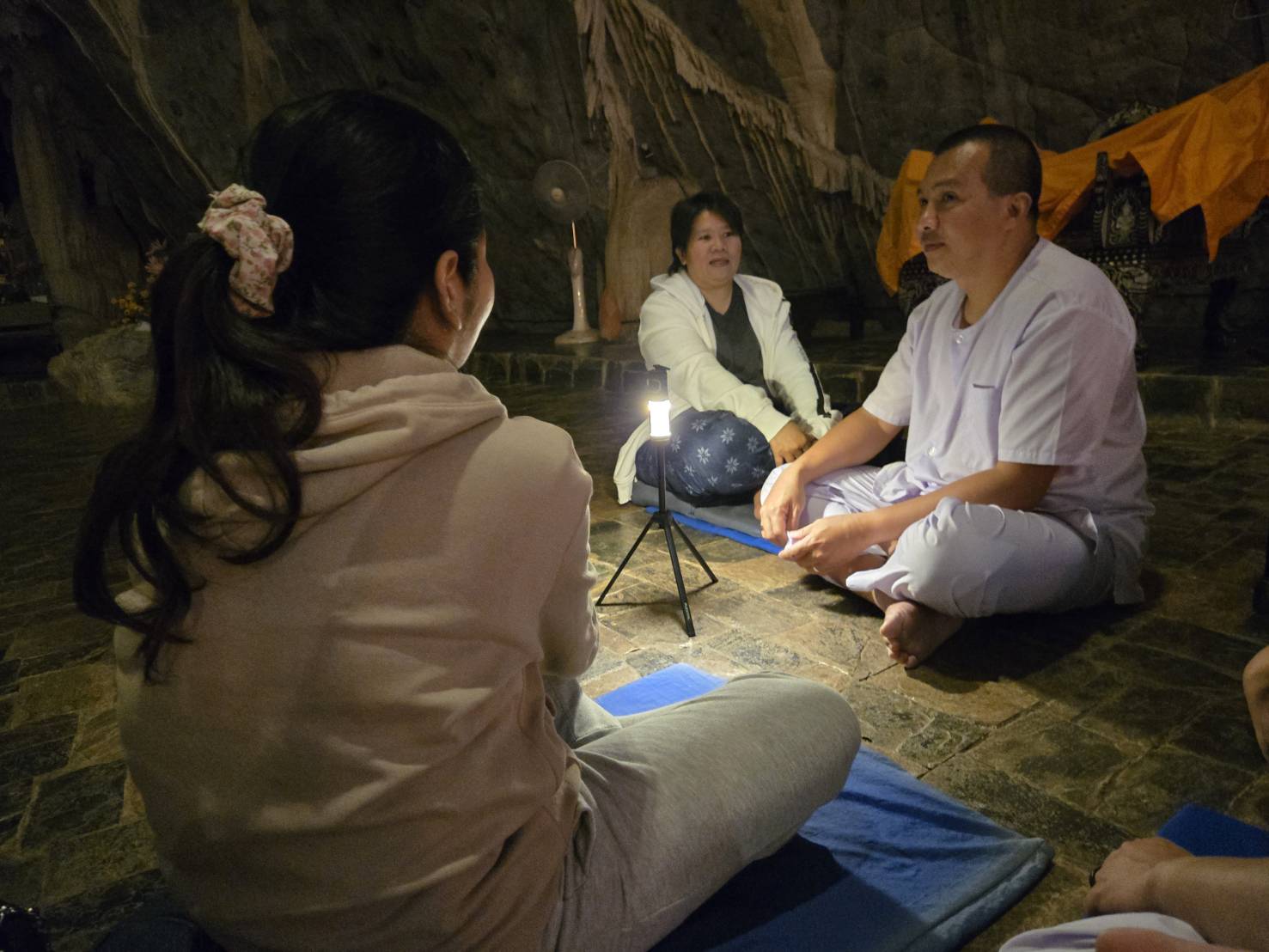 อาจารย์พี่เลี้ยงสนทนาธรรมกับผู้ปฏิบัติธรรมภายในถ้ำ ใช้แสงจากตะเกียงตั้งพื้น